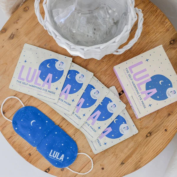 LULA self-warming eye mask packaging on a wooden surface with a blue mask.