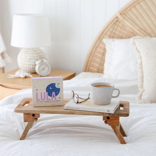 Wooden tray on a bed with a book, mug, and glasses, featuring the brand &