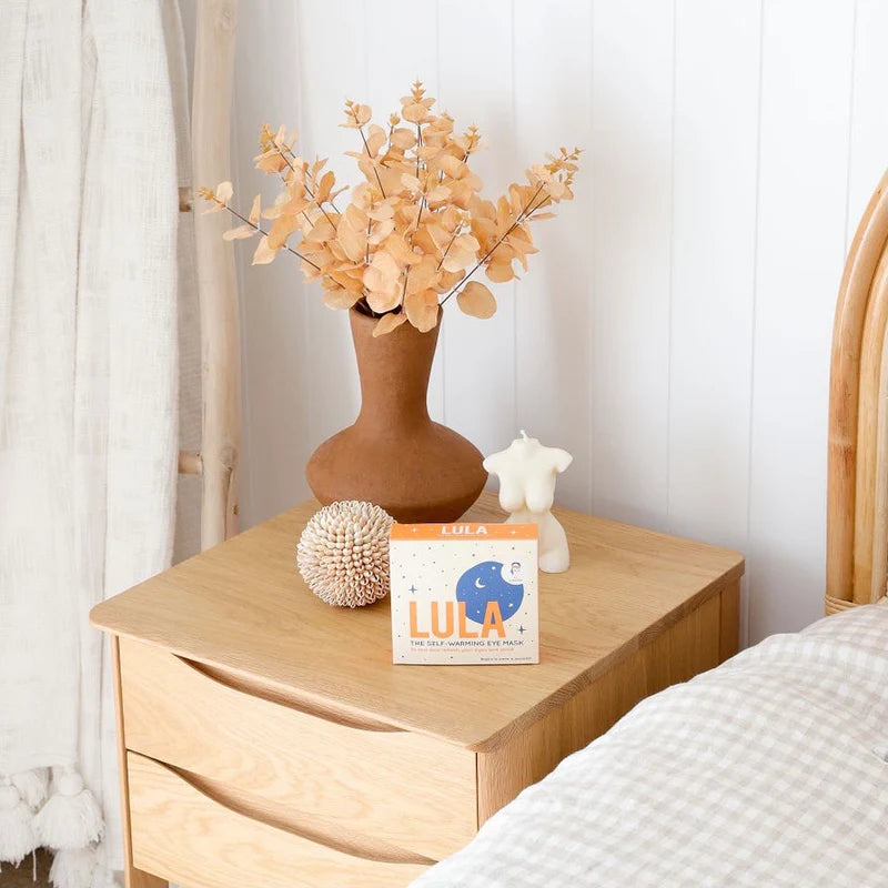 Wooden nightstand with decorative items including a vase with flowers, a box labeled &