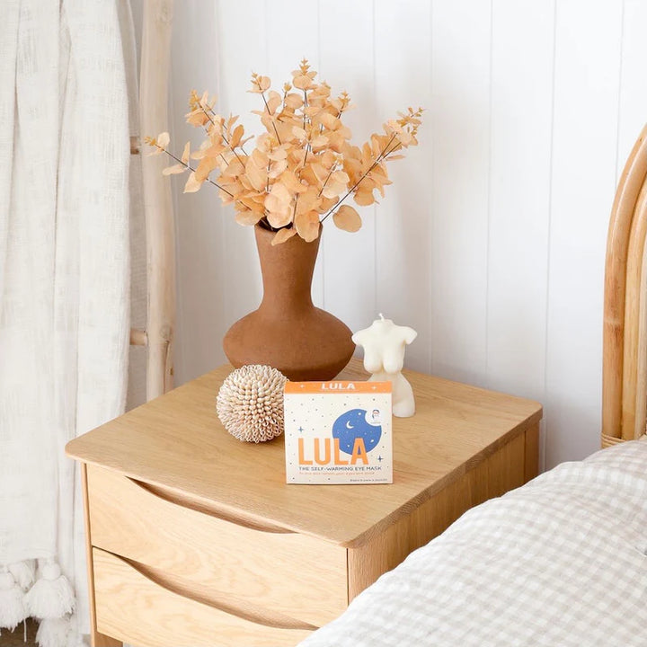 Wooden nightstand with decorative items including a vase with flowers, a box labeled &