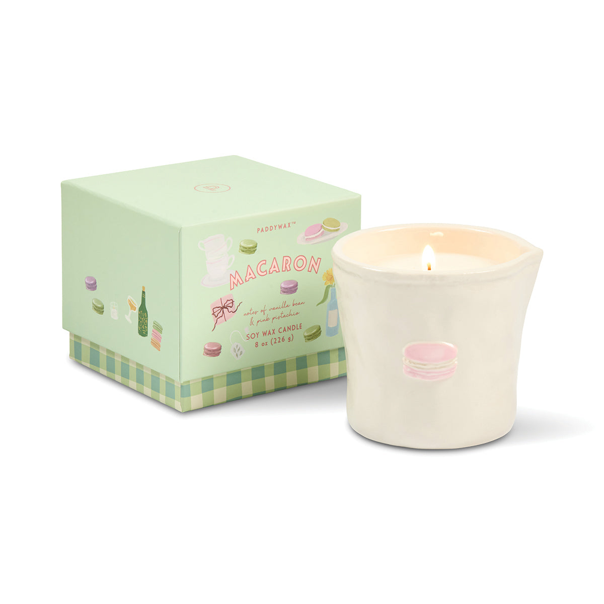 Candle with macaron design next to its packaging on a white background