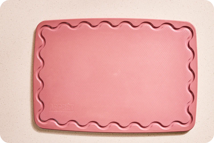 Pink cutting board with scalloped edge on a beige background