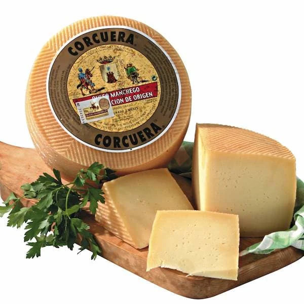 Round wheel of Manchego cheese with a few slices on a wooden board, featuring a visible brand label.