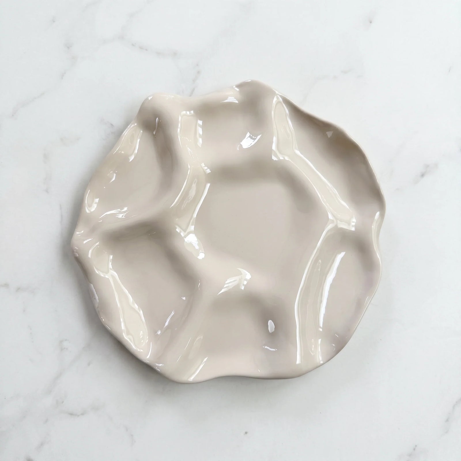 A glossy, wavy ceramic dish with multiple irregular compartments, shown on a white marble surface.