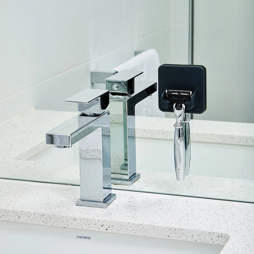 Bathroom basin with a grey silicone razor holder stuck to the mirror, holding a razor