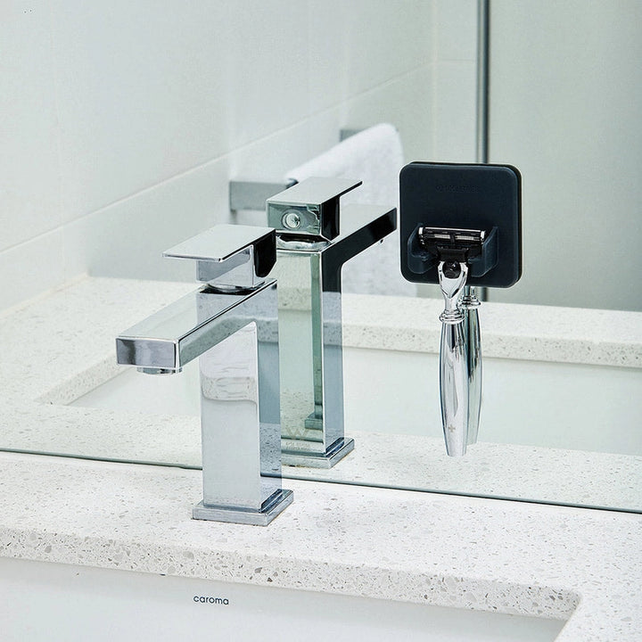 Bathroom basin with a grey silicone razor holder stuck to the mirror, holding a razor