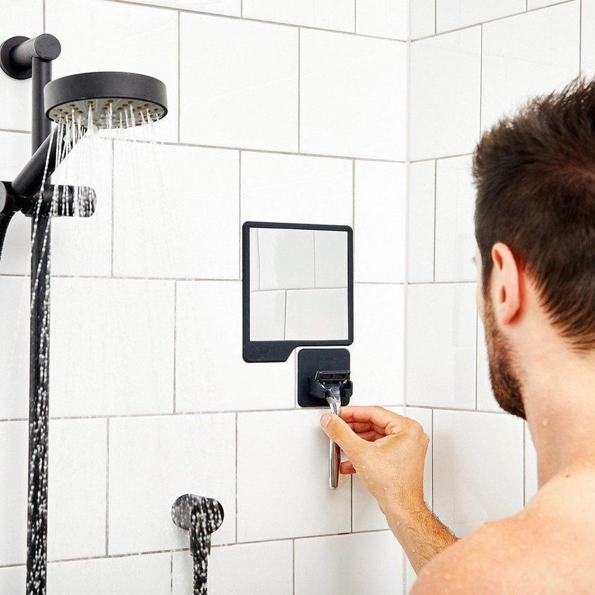 Man placing a razor into a grey silicone razor holder, attached to a white tiled wall in a shower