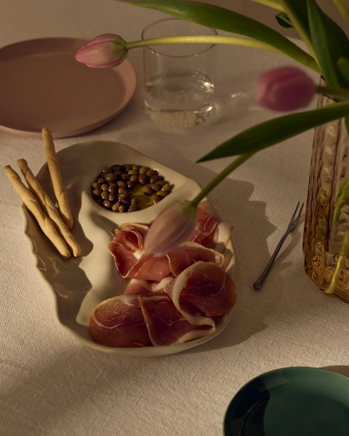 Plated meat with bread sticks and a glass of water on a table with a vase of flowers.
