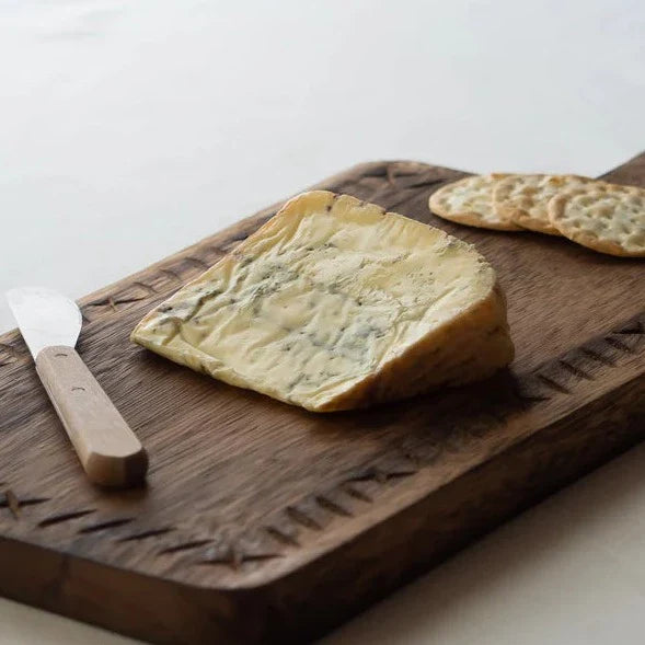 Slice of blue cheese on a wooden cutting board with a knife and crackers.