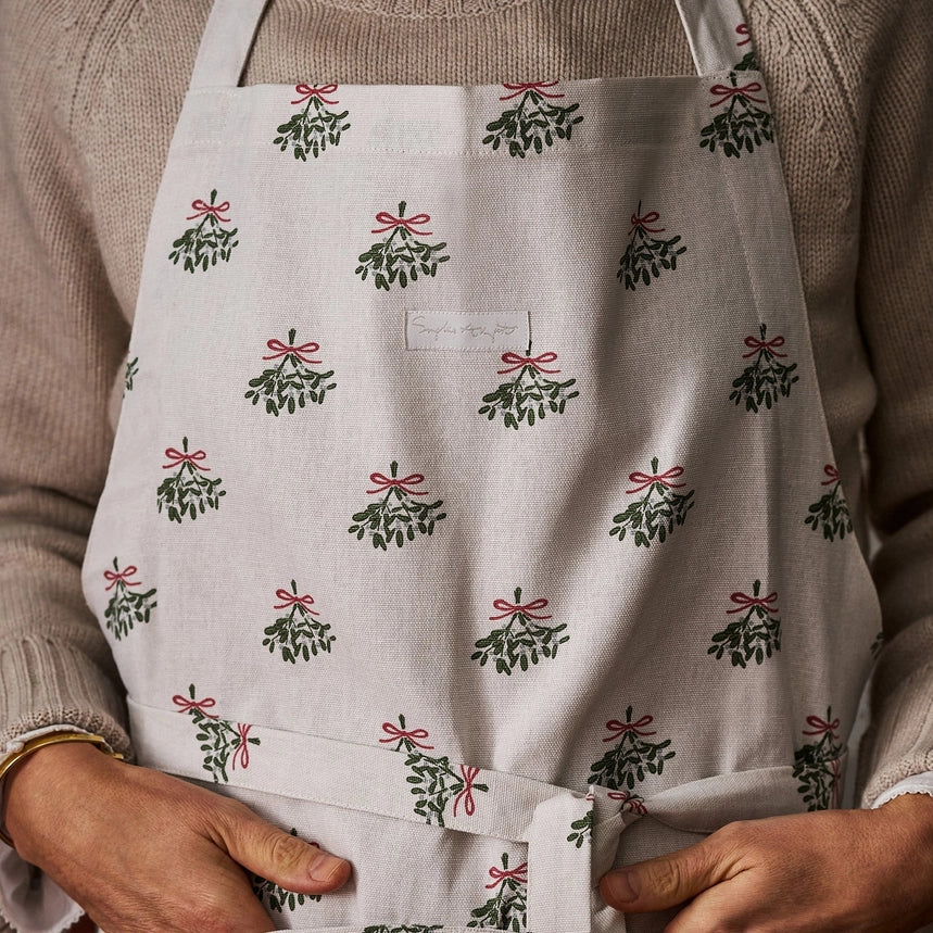 Cream cotton apron with a repeated mistletoe print on a person wearing a wool jumper