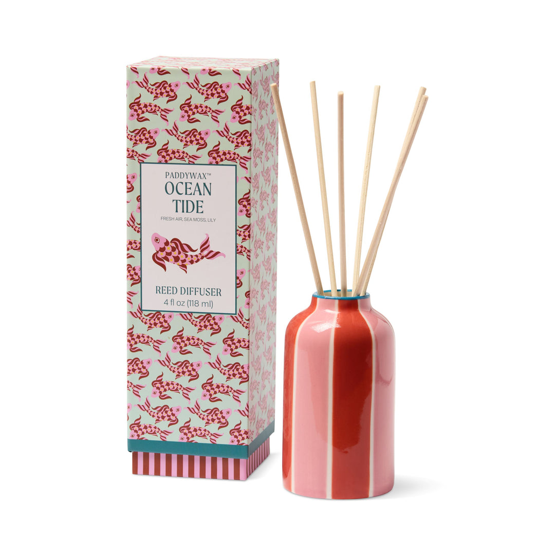 Paddywax Ocean Tide reed diffuser set with a glossy coral pink bottle, natural wooden reeds, and its patterned retail box on a white background.