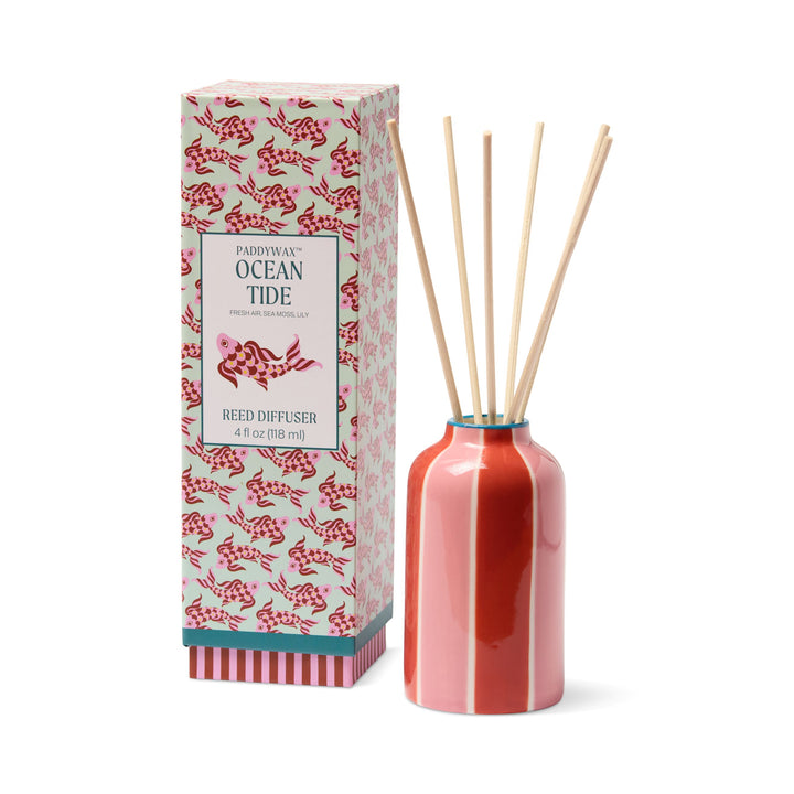 Paddywax Ocean Tide reed diffuser set with a glossy coral pink bottle, natural wooden reeds, and its patterned retail box on a white background.