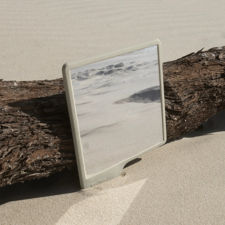 Sand coloured shower mirror in the sand leaning against driftwood