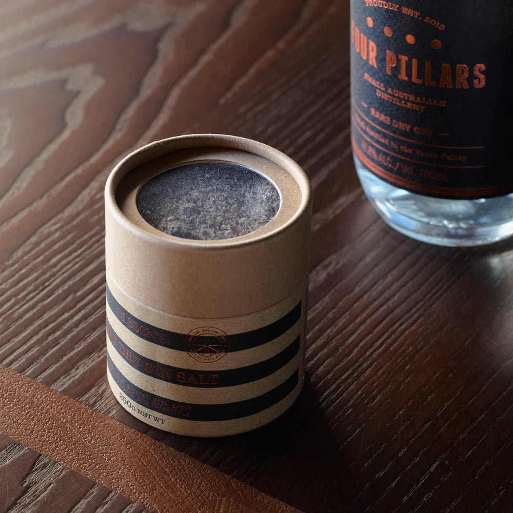 Cylindrical container with striped design on a wooden surface next to a bottle of Four Pillars gin.