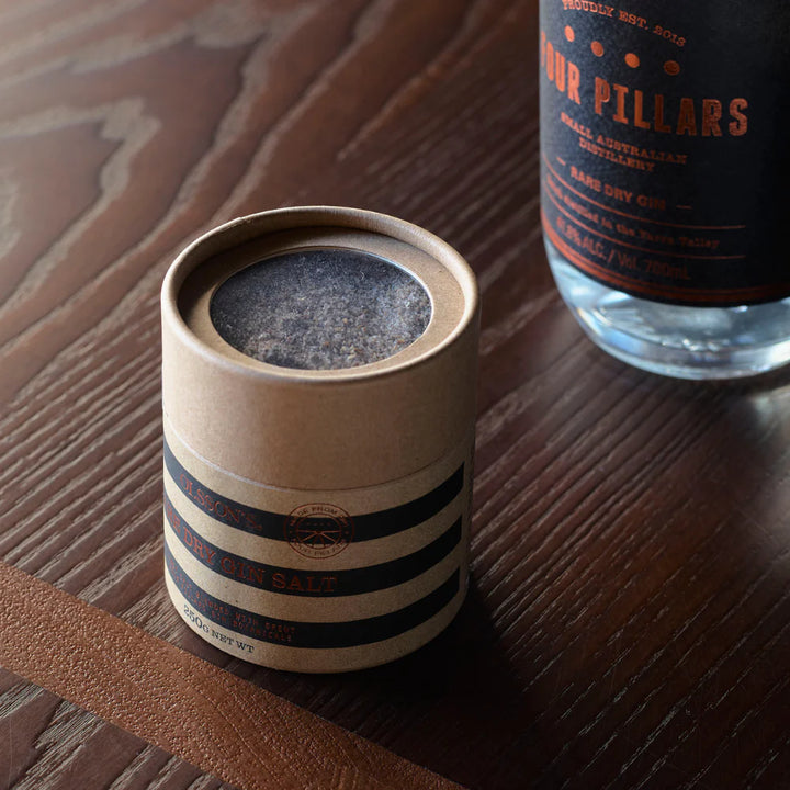 Cylindrical container with striped design on a wooden surface next to a bottle of Four Pillars gin.