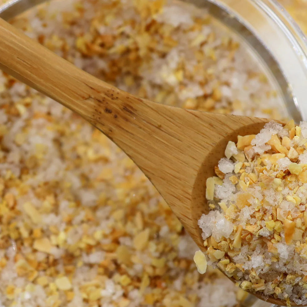 Wooden spoon filled with a mixture of yellow and white granules, possibly salt and flowers, over a container.