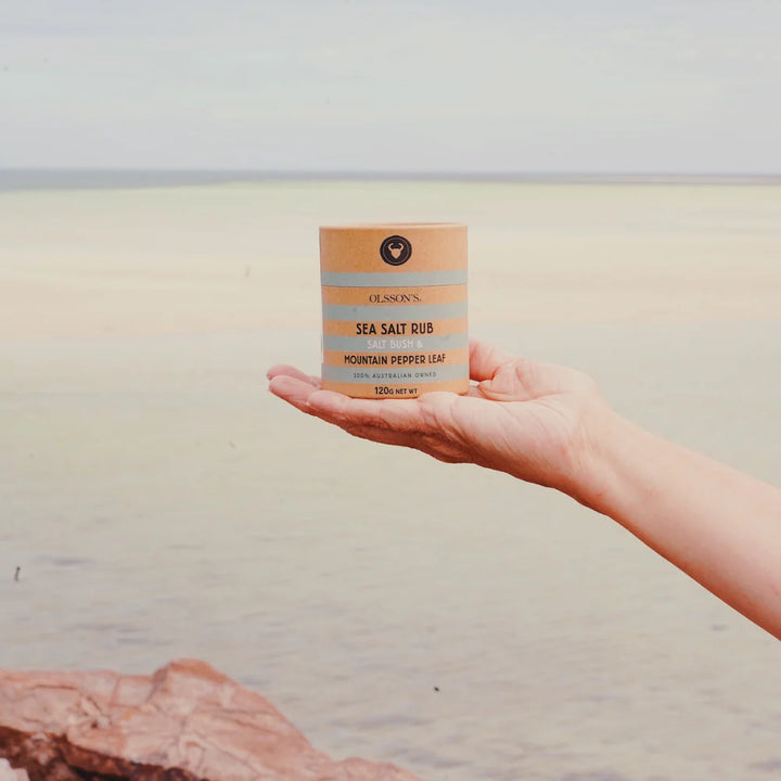 Hand holding a box of sea salt rub against a beach background