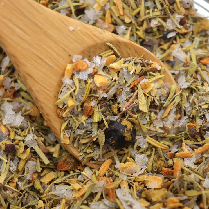 Wooden spoon filled with a mix of dried herbs and spices on a bed of similar herbs.