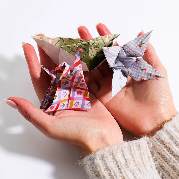 Three small origami paper birds in different colorful patterns are held in two hands against a clean white background.