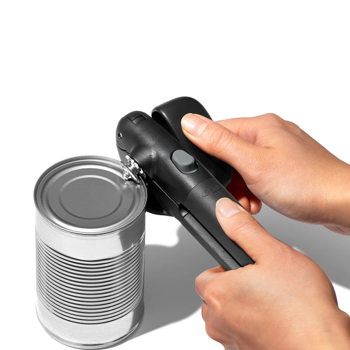 Hand using a can opener on a can against a white background