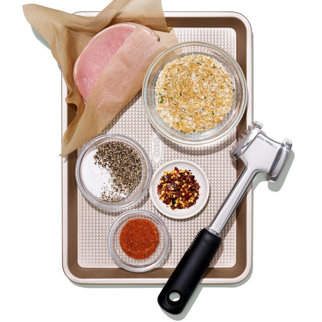 Pork medallion with spices and crumbs and a tenderizer on a tray