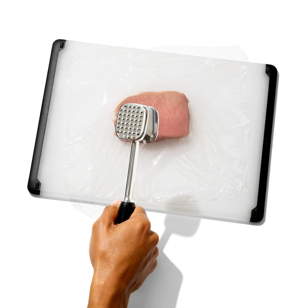Hand holding a meat tenderizer over a block of meat on a white background