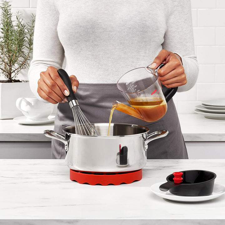 Person cooking in a kitchen with a pot on a hot plate, whisk, and fat separator jug