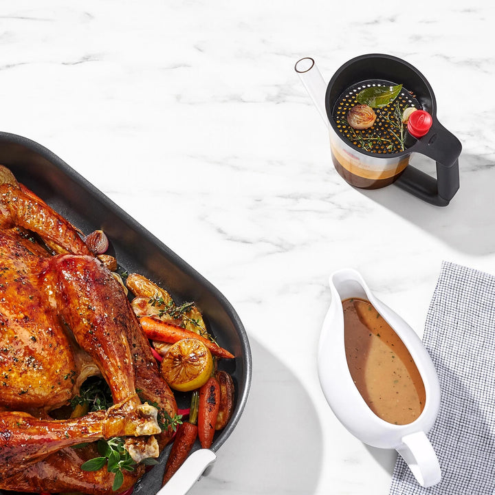 Roasted turkey with vegetables on a white marble surface, accompanied by a pitcher of gravy and a fat separator jug