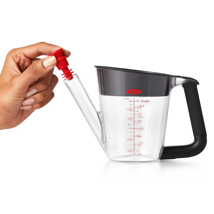 Hand holding a measuring cup with a red spout on a white background