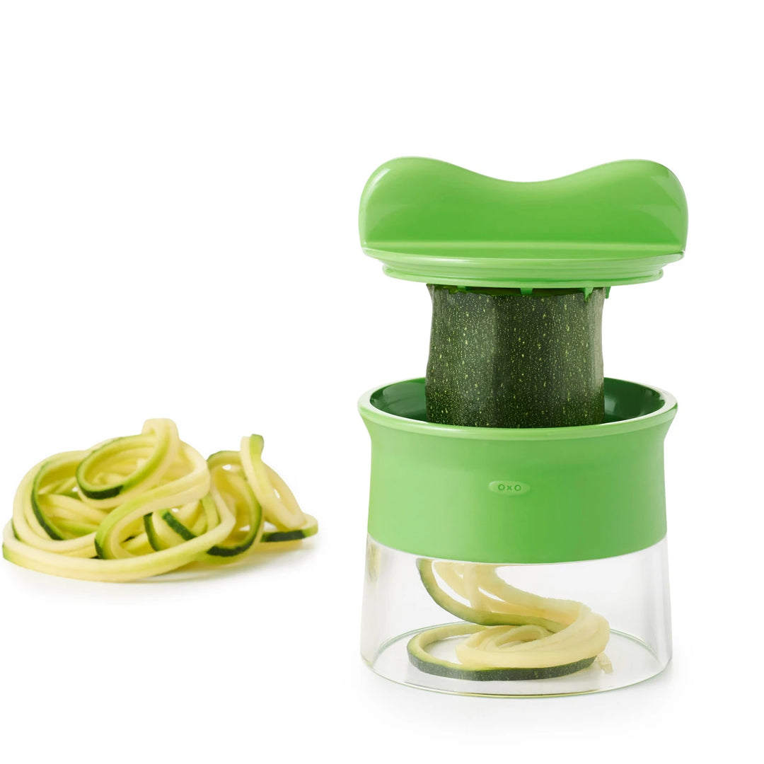 Green spiralizer with zucchini noodles on a white background