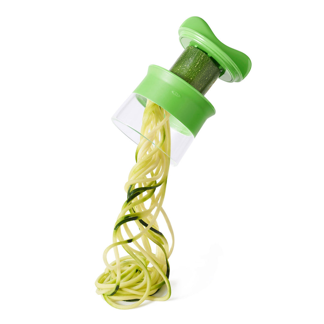 Zucchini being spiralized into noodles using a green spiralizer on a white background