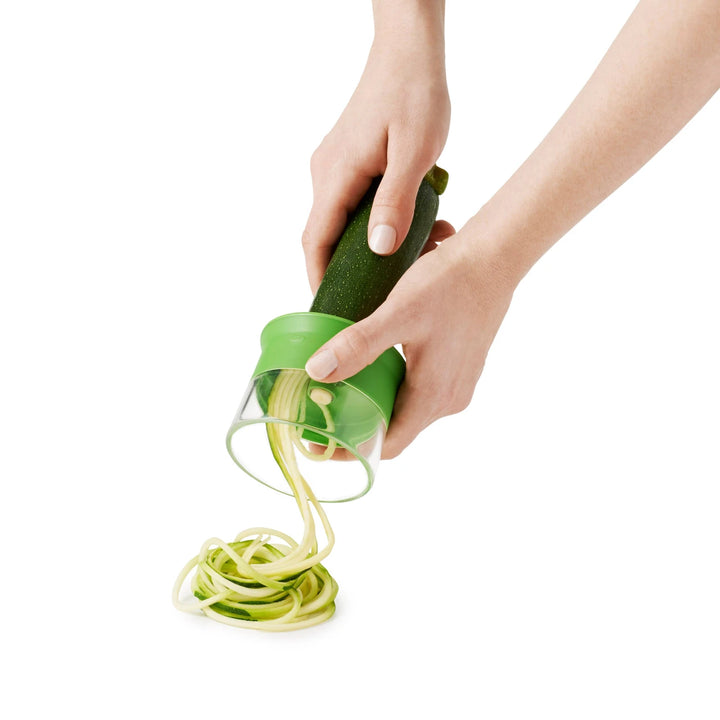 Green spiralizer being used to create zucchini noodles on a white background