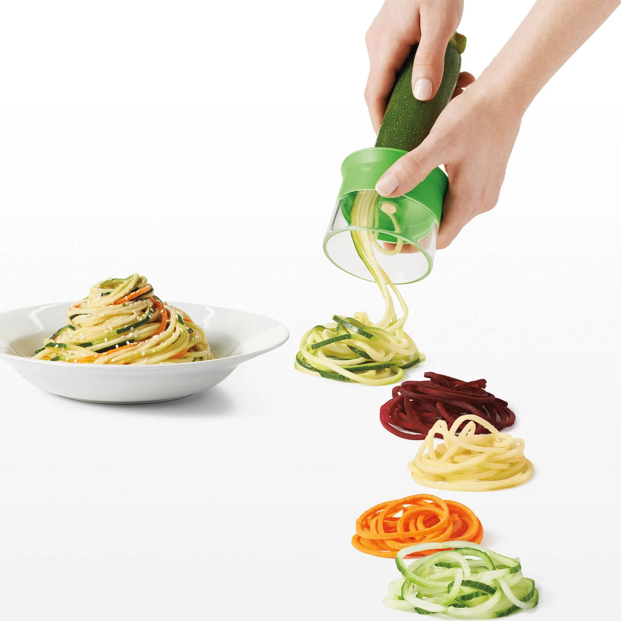 Hand using a spiralizer to create colorful zucchini noodles on a white background