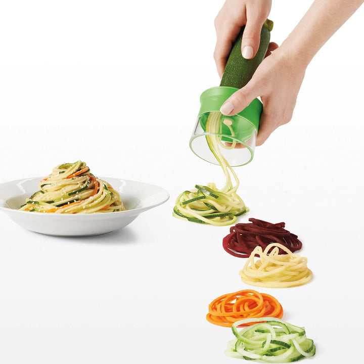 Hand using a spiralizer to create colorful zucchini noodles on a white background