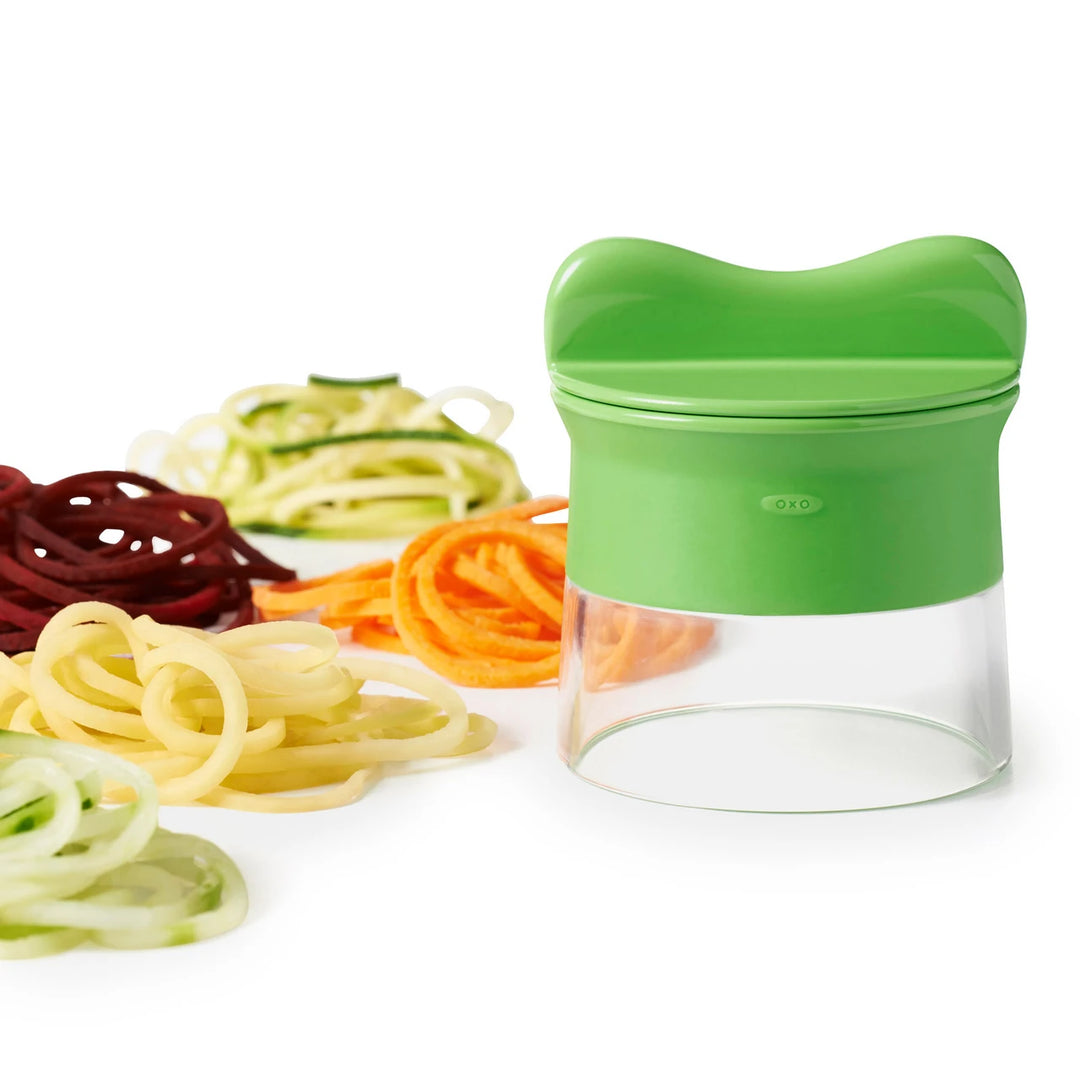 Green spiralizer with various spiralized vegetables on a white background