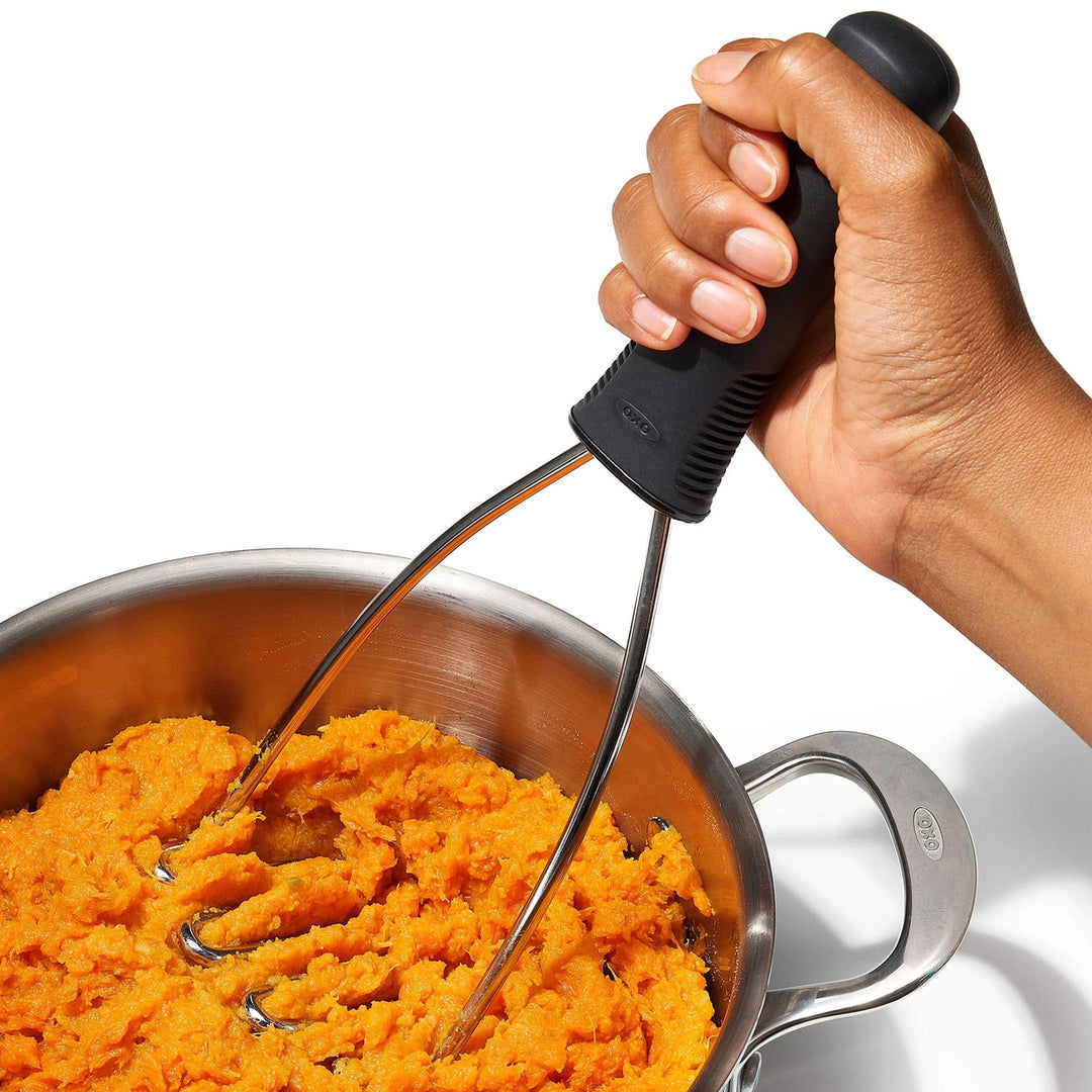 Hand using a potato masher to mash sweet potatoes in a pot.