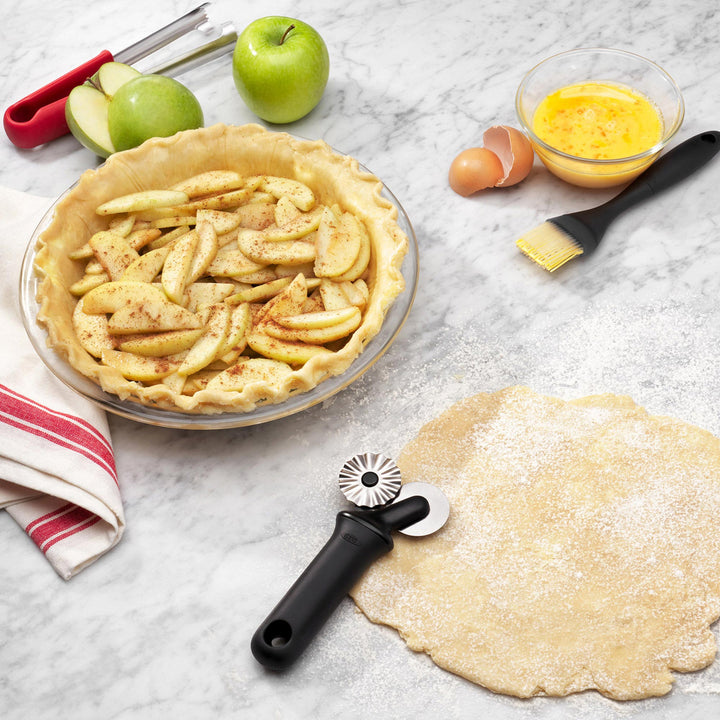 Apple pie with ingredients and a pie cutter and pastry brush on a marble surface