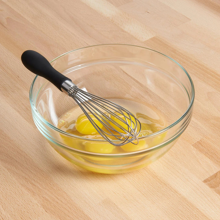 Clear glass bowl with whisk and eggs on a wooden surface