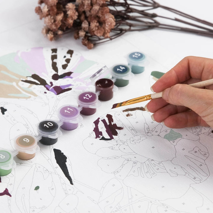Person painting a coloring book with watercolor paints and a brush.