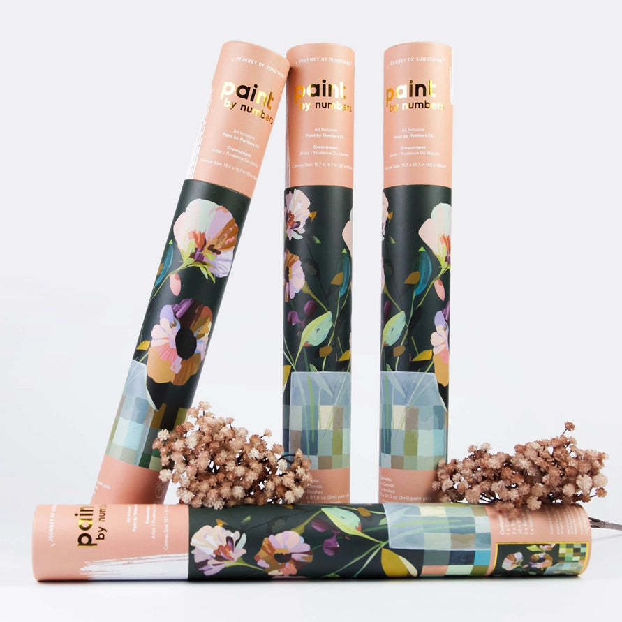 Three rolled paint by numbers with peach paper sleeves and dark floral-patterned bottoms are arranged on a white background, with dried flower sprigs in front. The text on the rolls reads &