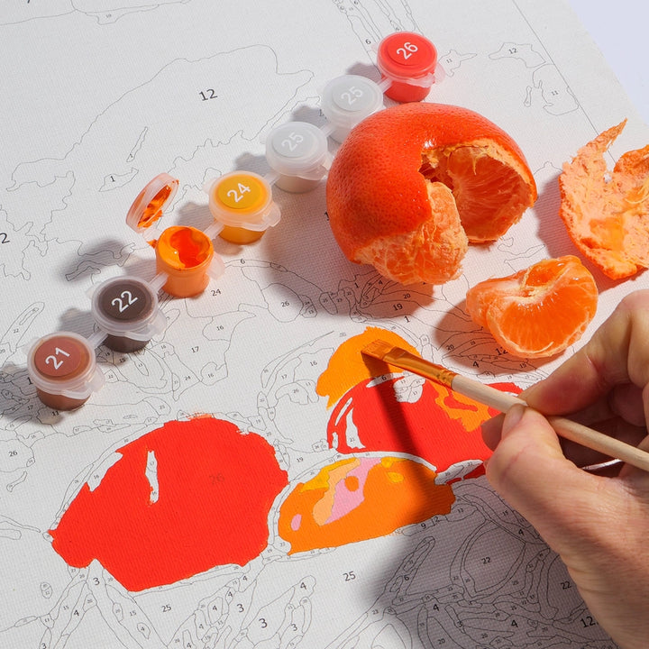 Person painting with orange paint on a paper with a mandarin orange and peels.