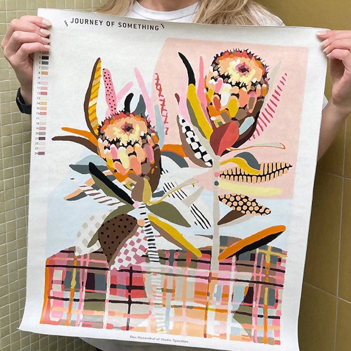 A person holds up a large art print featuring an abstract floral illustration with the title &