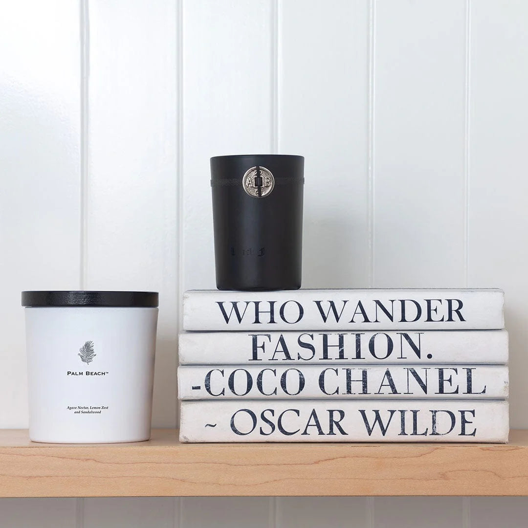 Stack of books with quotes and two candles on a shelf against a white paneled wall.