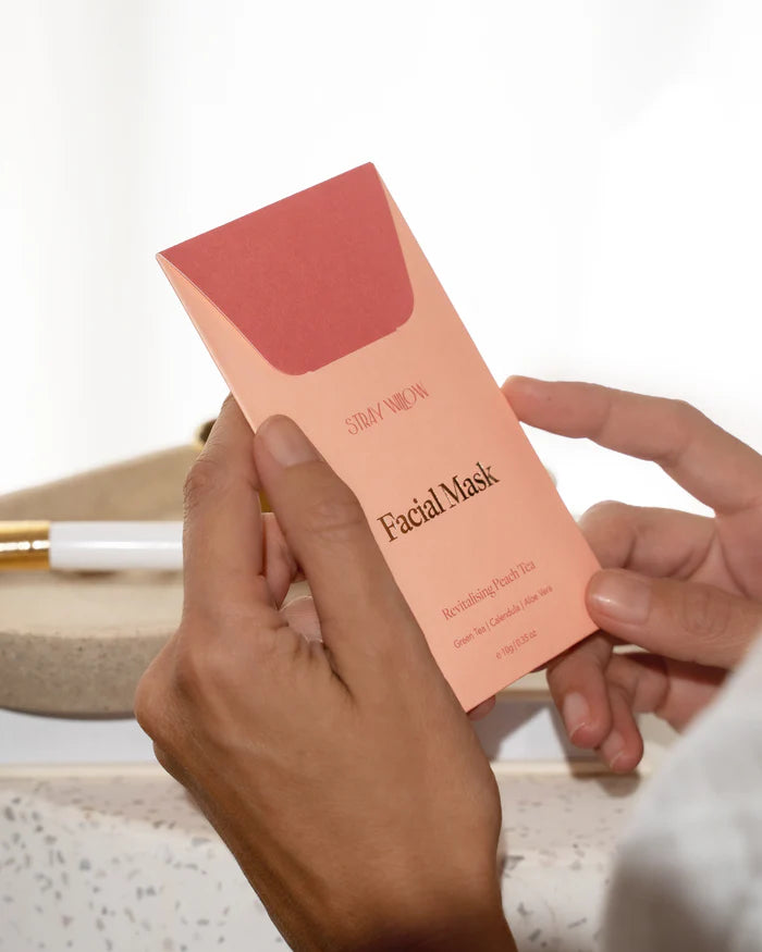 Hand holding a pink facial mask packaging with &