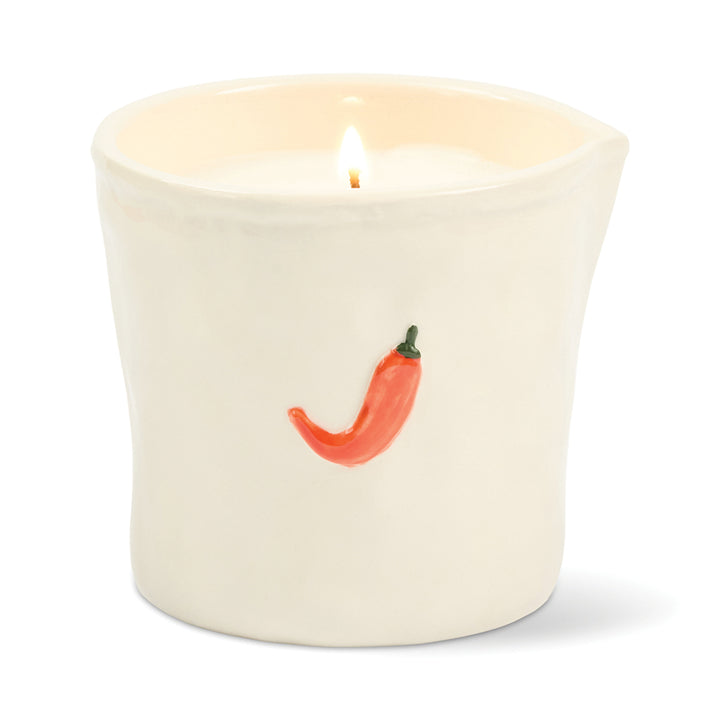 Candle in a white ceramic container with a red chili pepper design on a white background