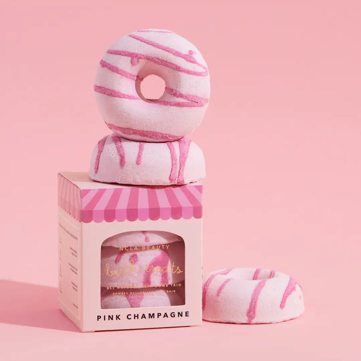 Pink and white striped donut-shaped bath bombs with packaging on a pink background