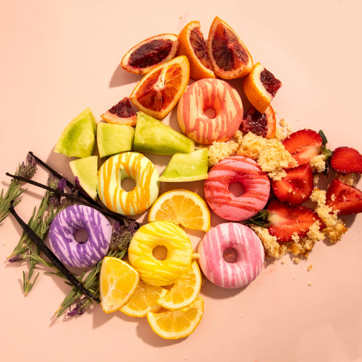 Colorful fruit and donut-shaped bath bombs arranged on a pink background