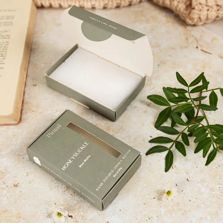 Two boxes of 'Honeysuckle' wax melts  on a textured surface with green leaves and flowers.