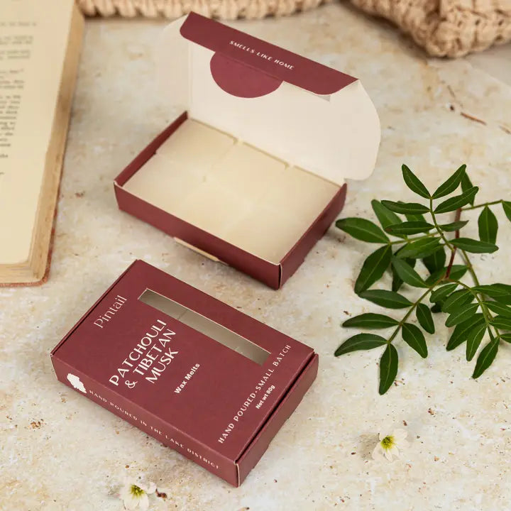 Red box with a window, open to reveal a white wax melts, on a textured surface with green leaves and a book.