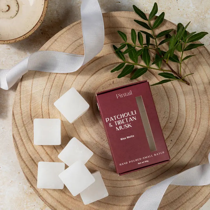 Pintail Patchouli &amp; Tibetan Musk wax melts packaging on a wooden surface with wax melts and greenery.